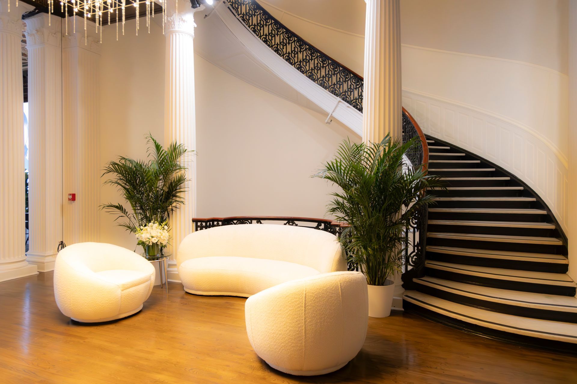 Elegant lobby with curved staircase, white lounge seating, potted plants, and warm lighting