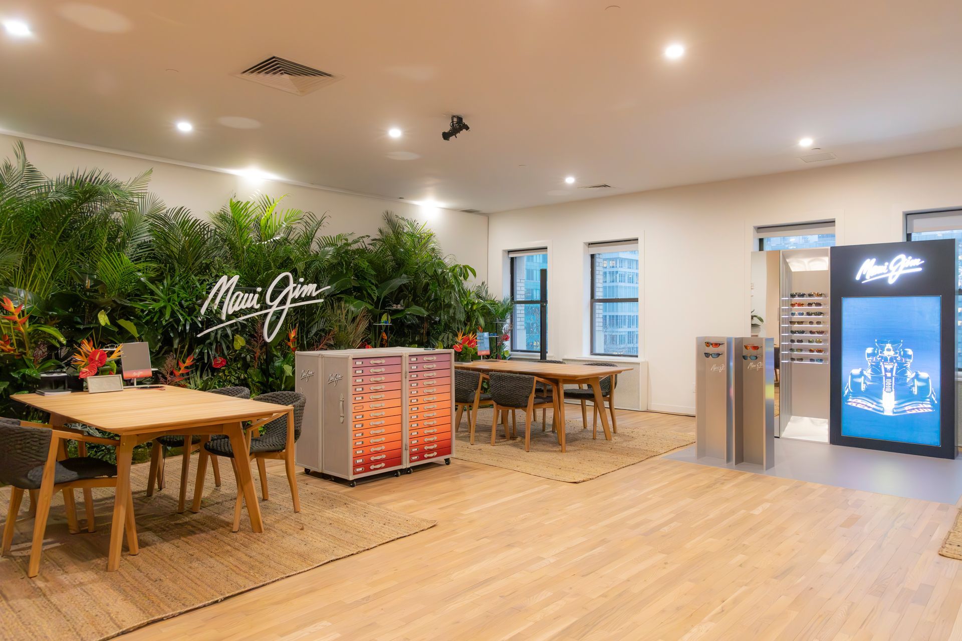 Bright modern lounge with wooden tables, greenery wall, and a glowing beverage cooler