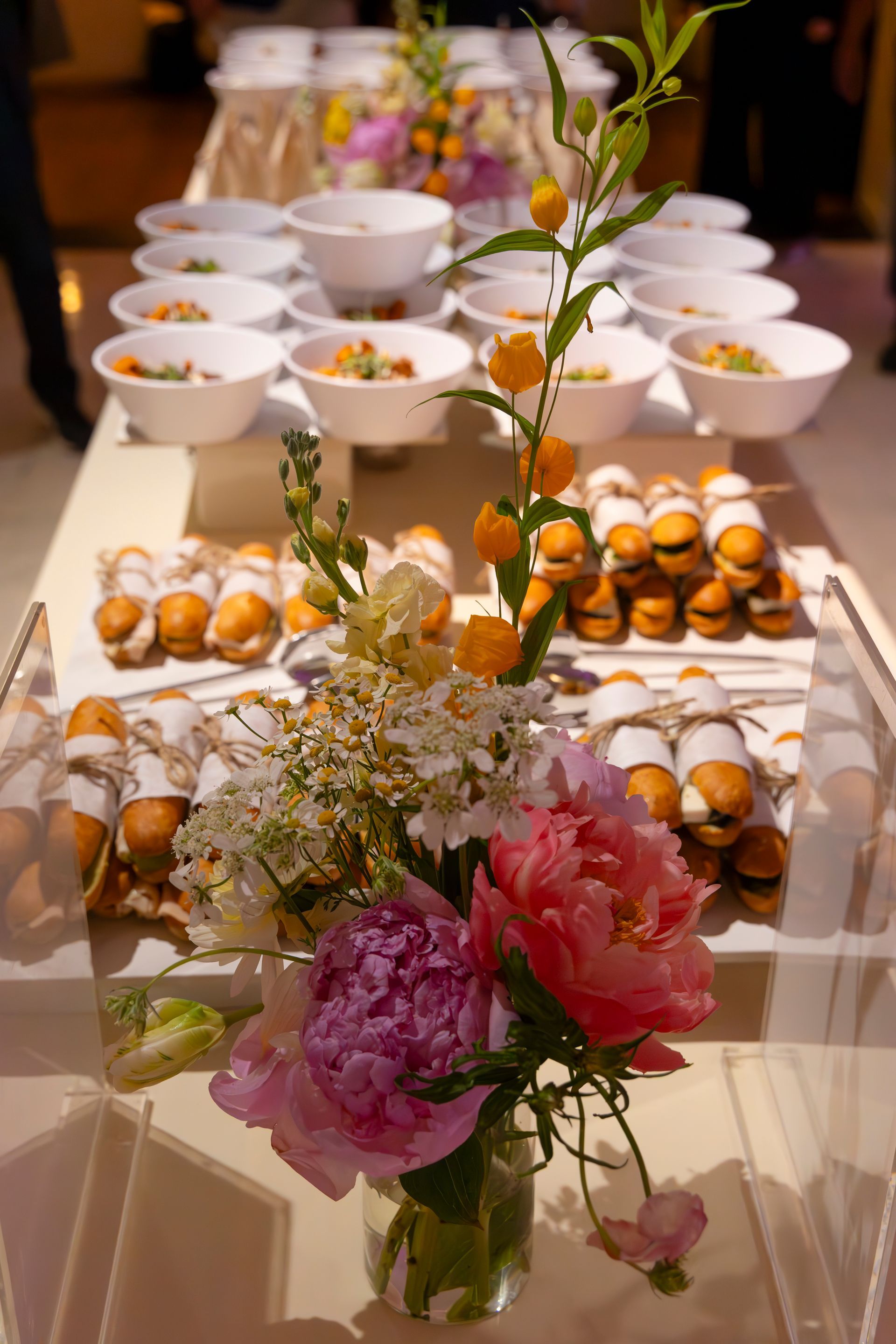 Buffet table with bowls of food and pastry trays, decorated with pink flowers in front