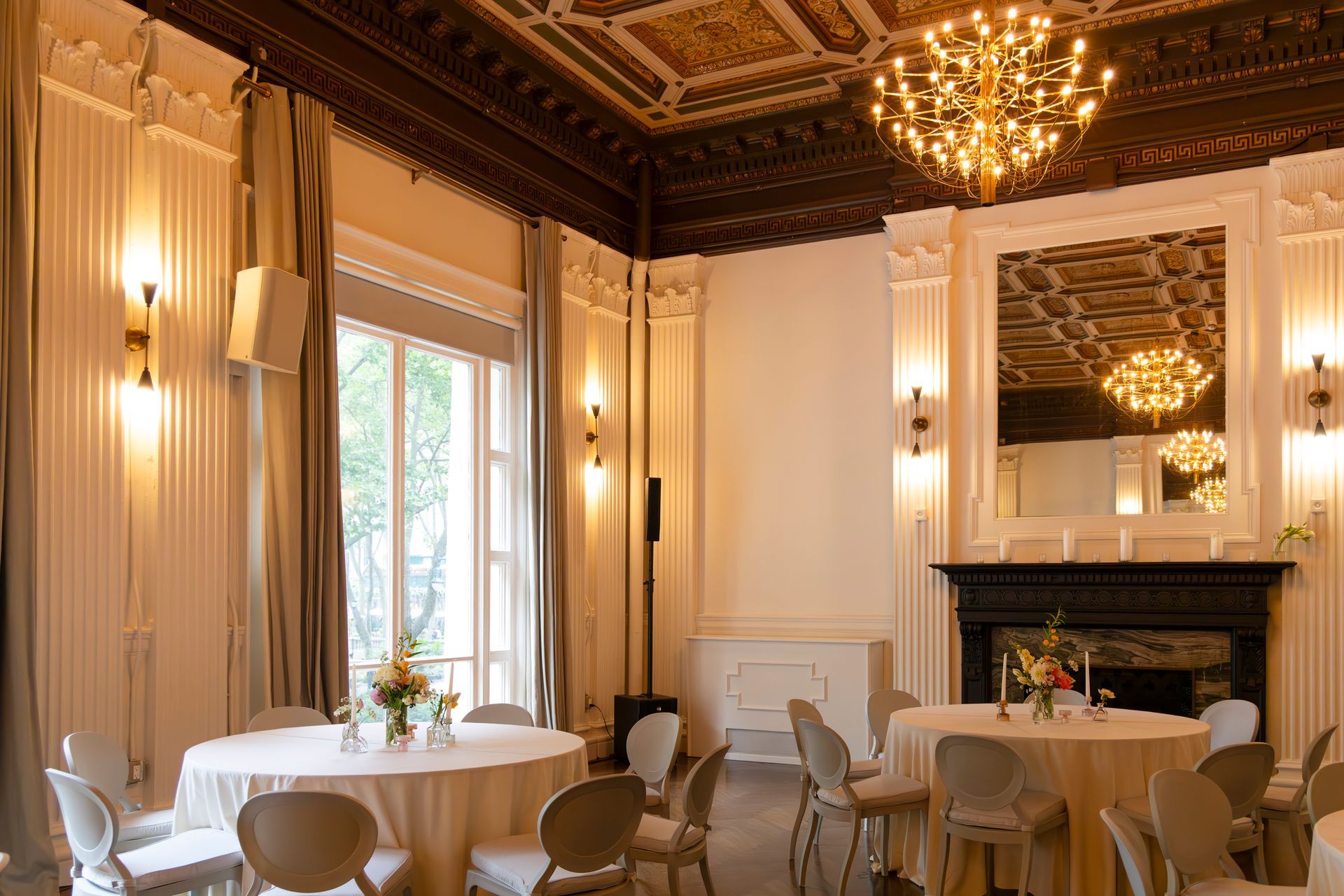 Elegant dining room with ornate gold ceiling, chandelier, fireplace, and round tables set with white tablecloths