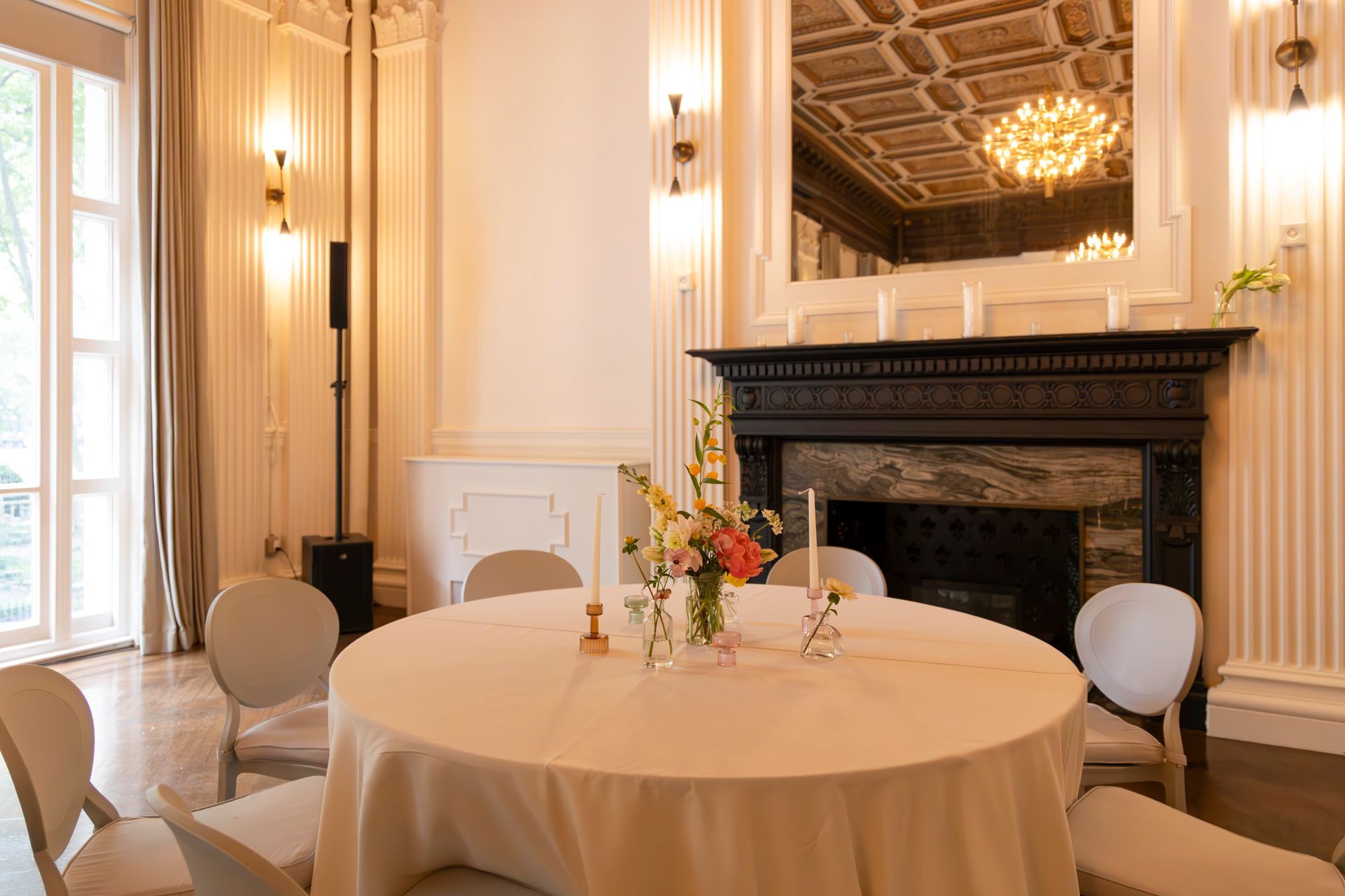 Elegant dining room with a round table, floral centerpiece, and fireplace under a gilded mirror