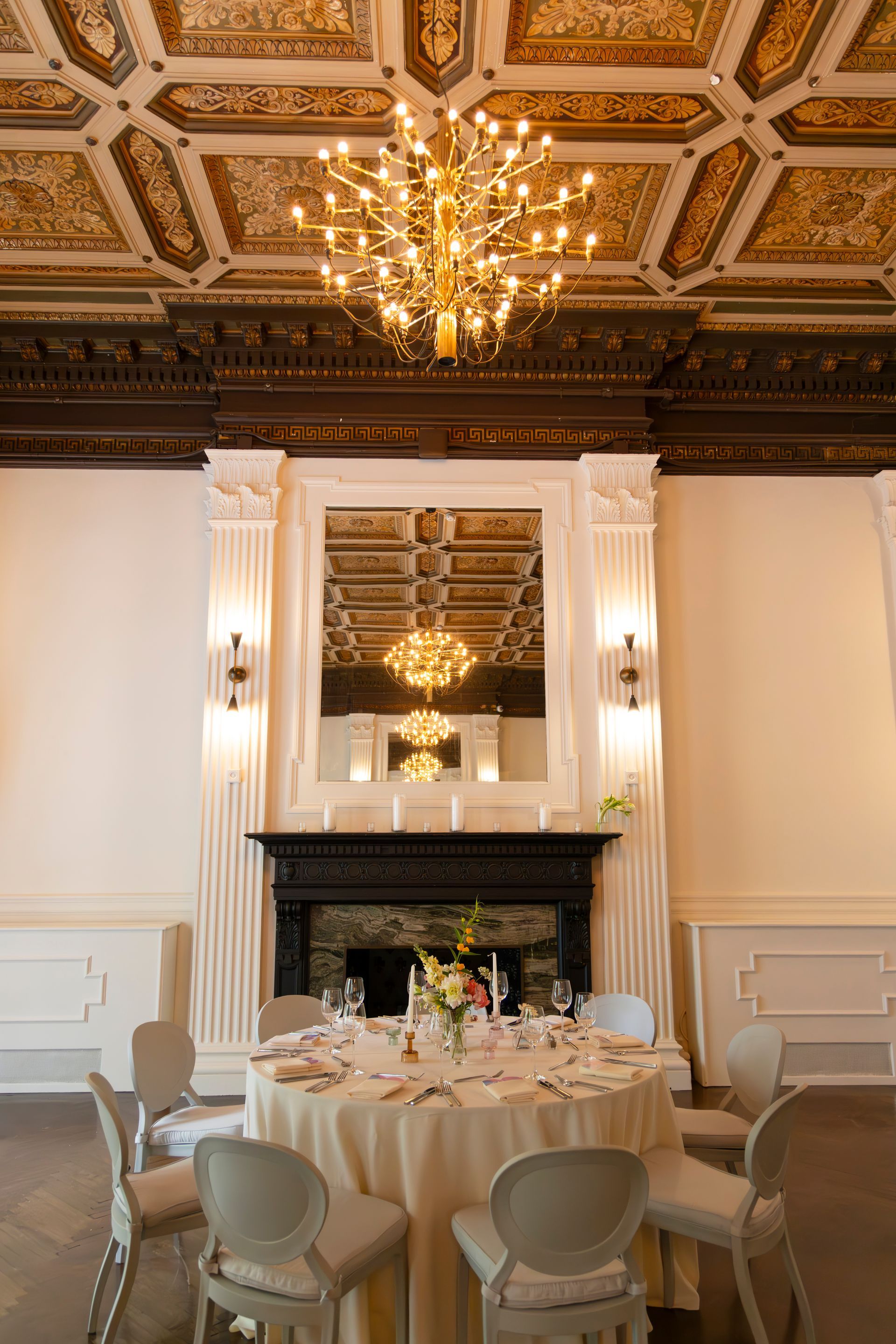 Elegant dining room with chandelier, ornate gold ceiling, mirror, and round table set for a formal meal