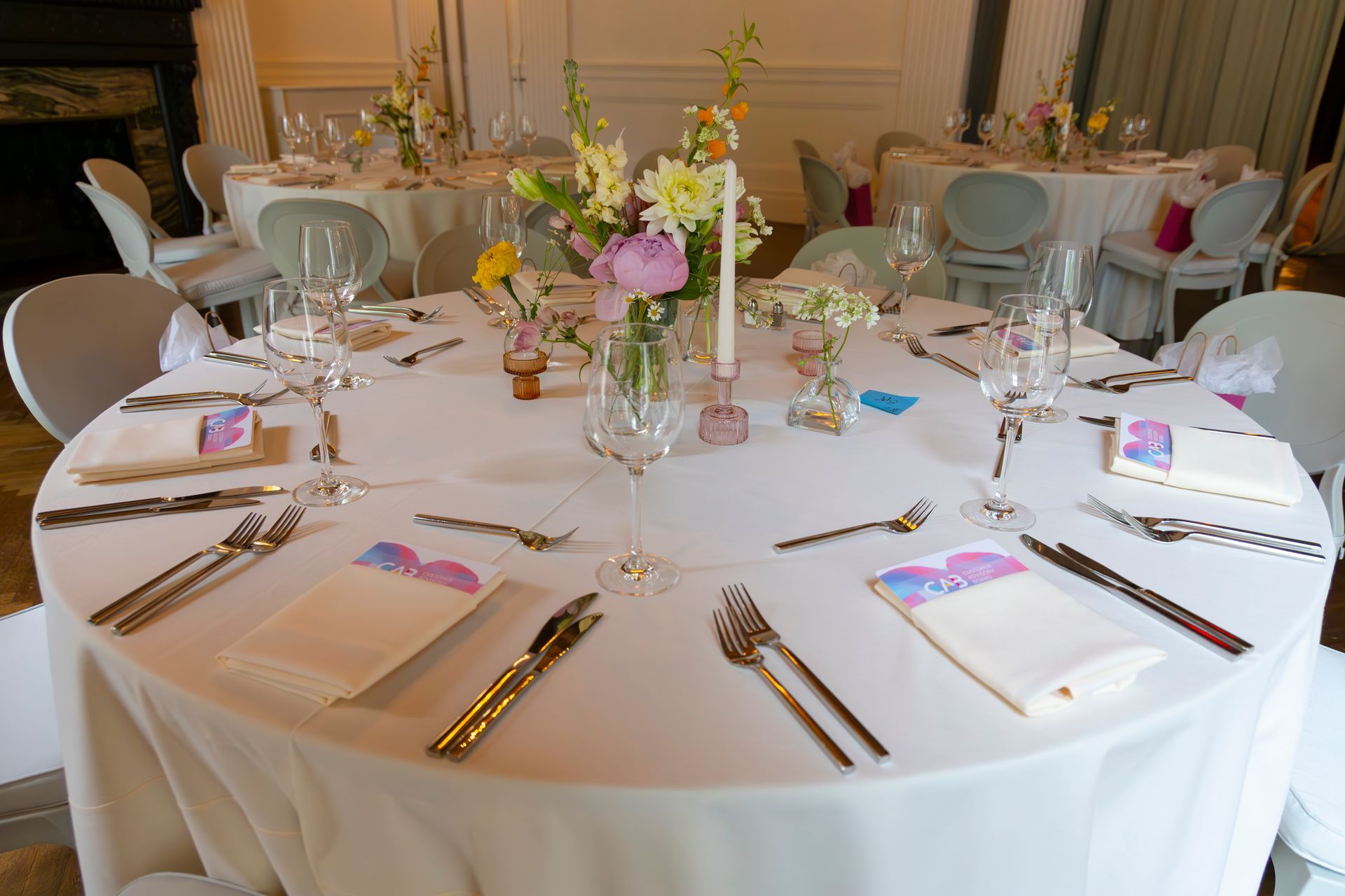 Round banquet table set with white linens, gold flatware, glassware, and pastel floral centerpieces