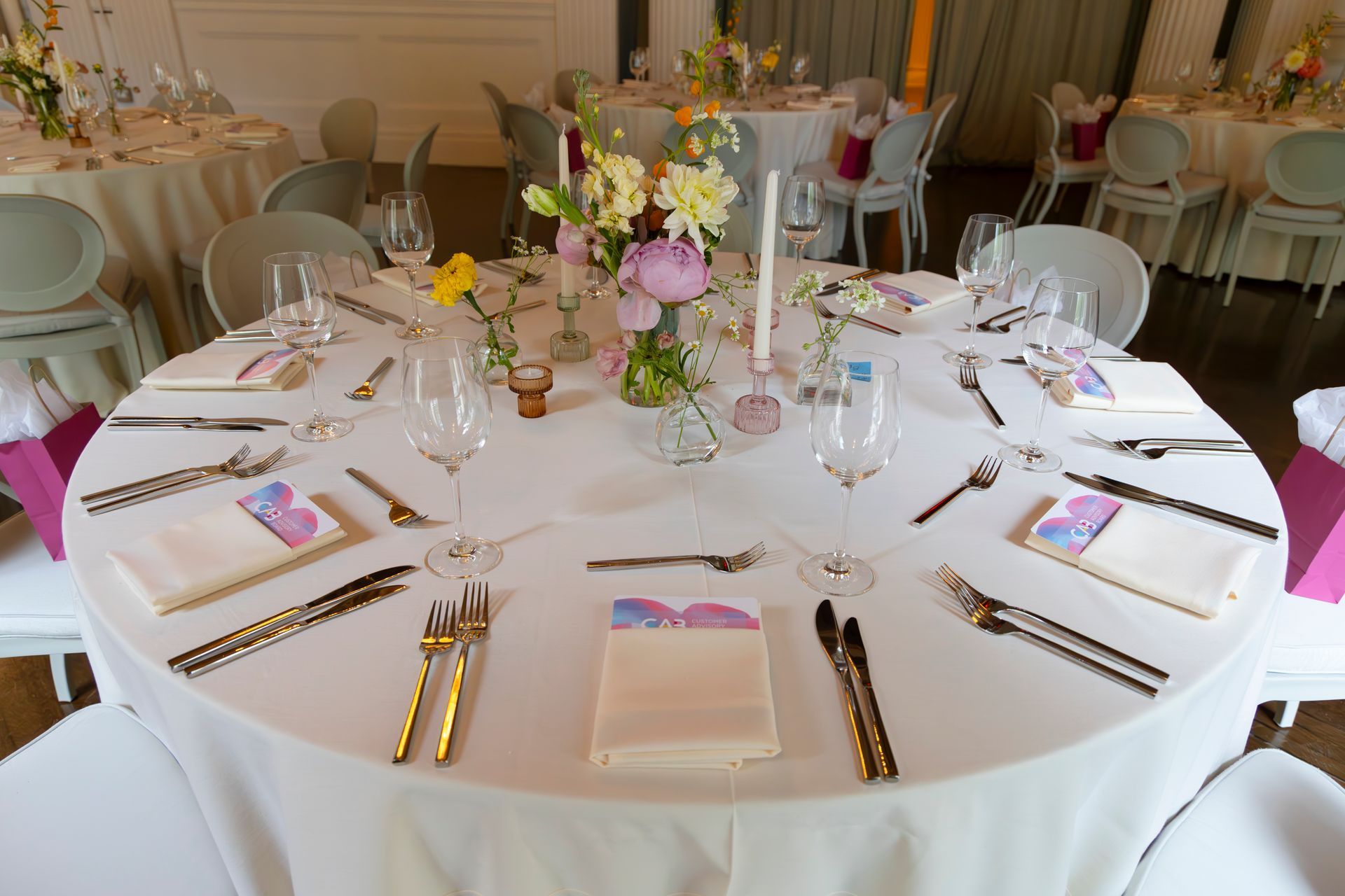 Round banquet table set with white linens, pink floral centerpiece, and gold cutlery in a formal dining room