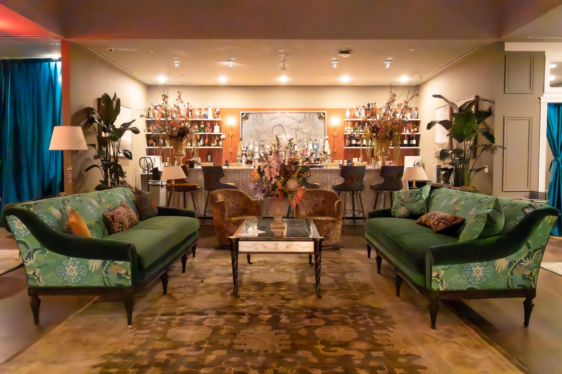 Elegant living room with green sofas, coffee table, and warm lighting overlooking a dining area