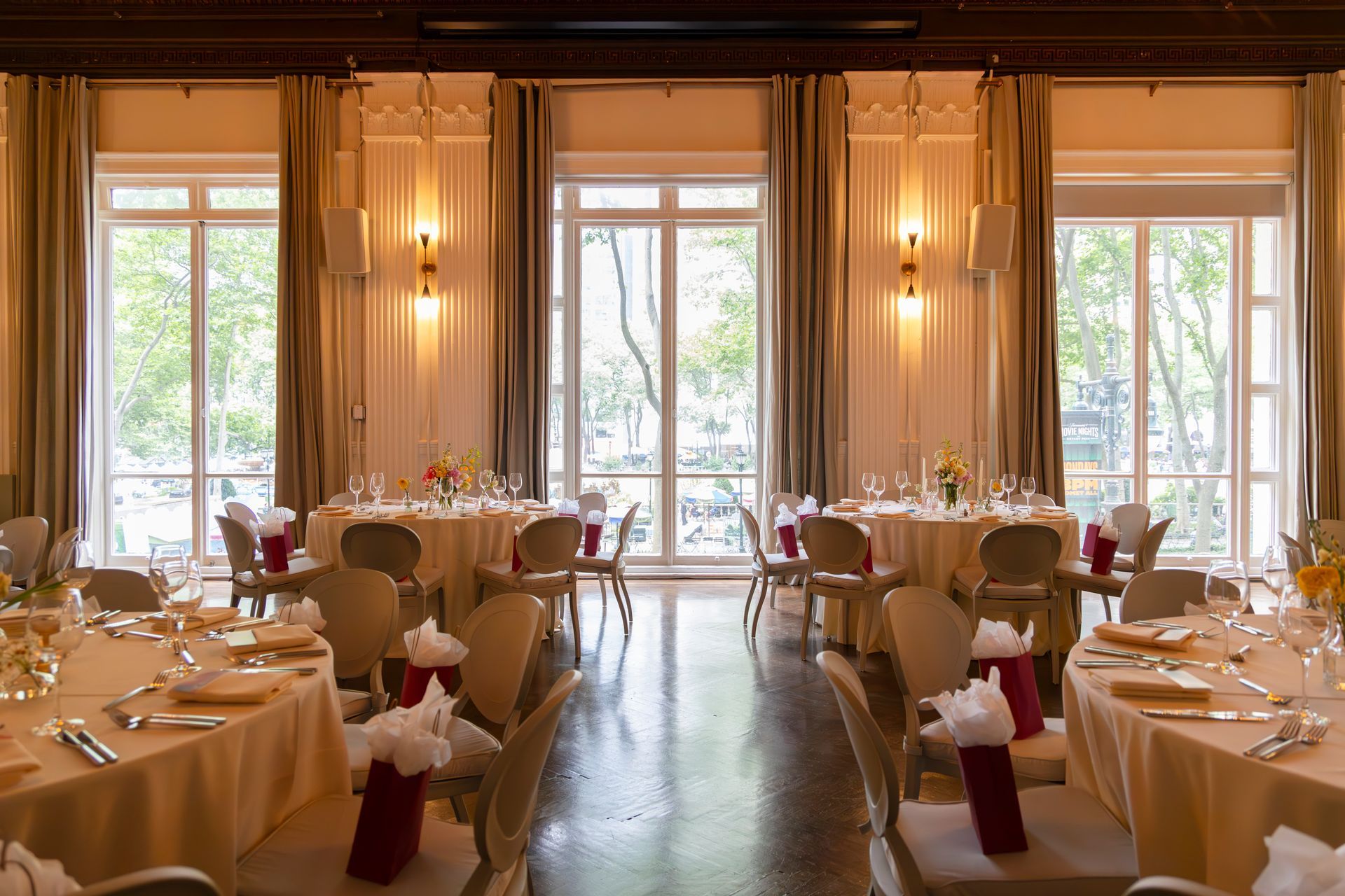 Elegant dining room with set tables, white drapes, and tall windows overlooking greenery