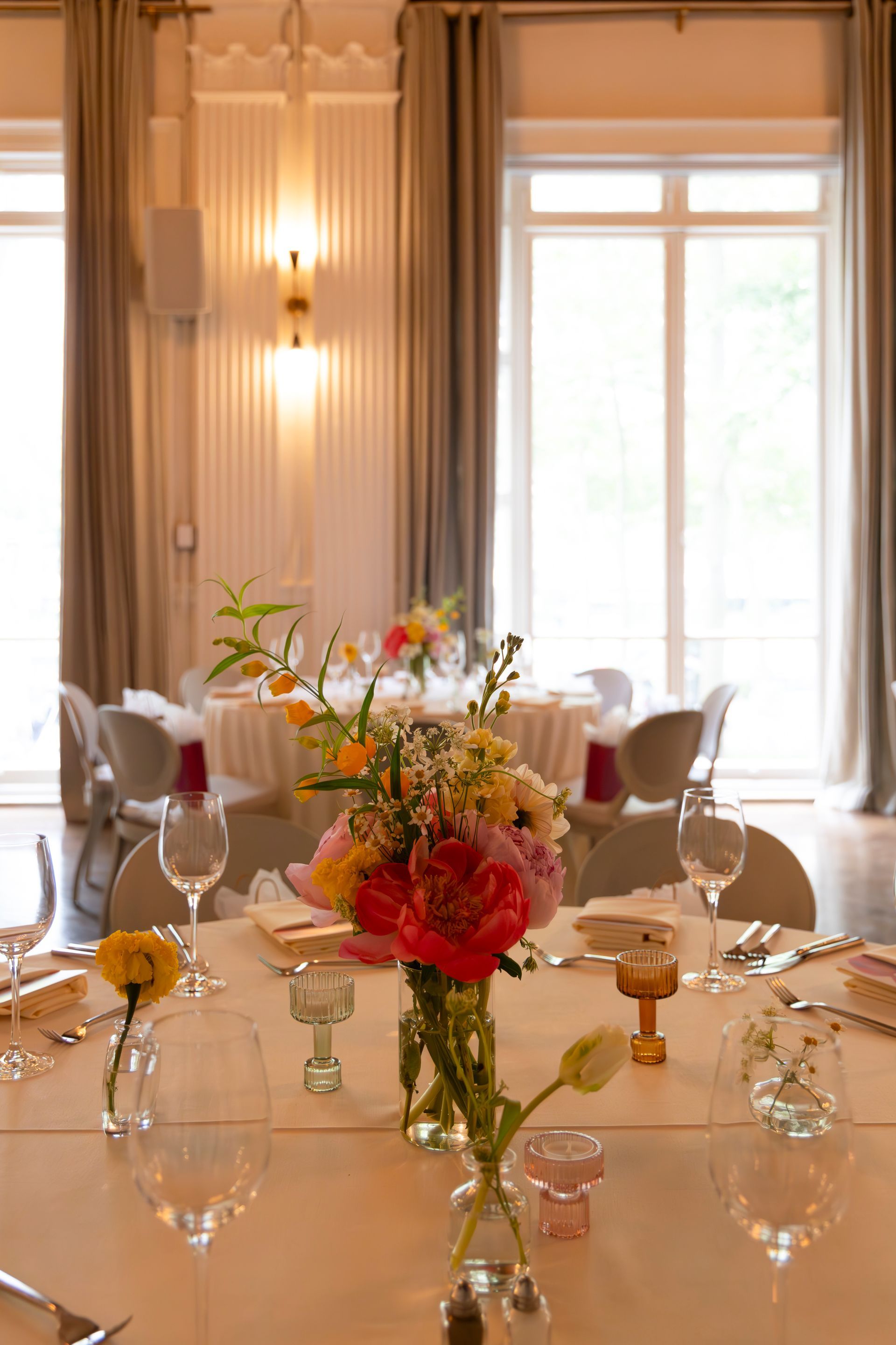 Elegant banquet table set with flowers, wine glasses, and candles in a bright formal dining room.