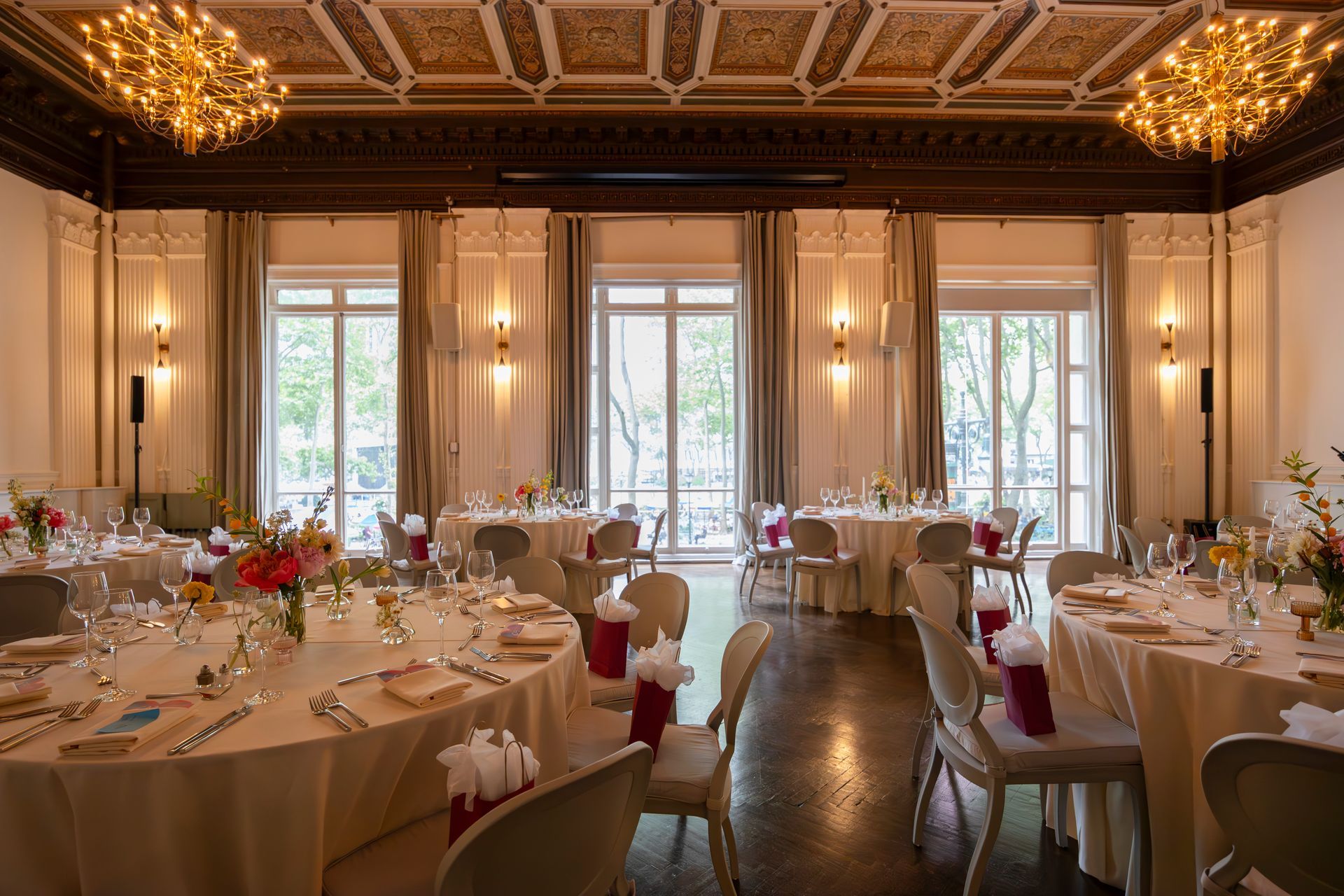 Elegant banquet hall with round tables, white tablecloths, floral centerpieces, and tall windows