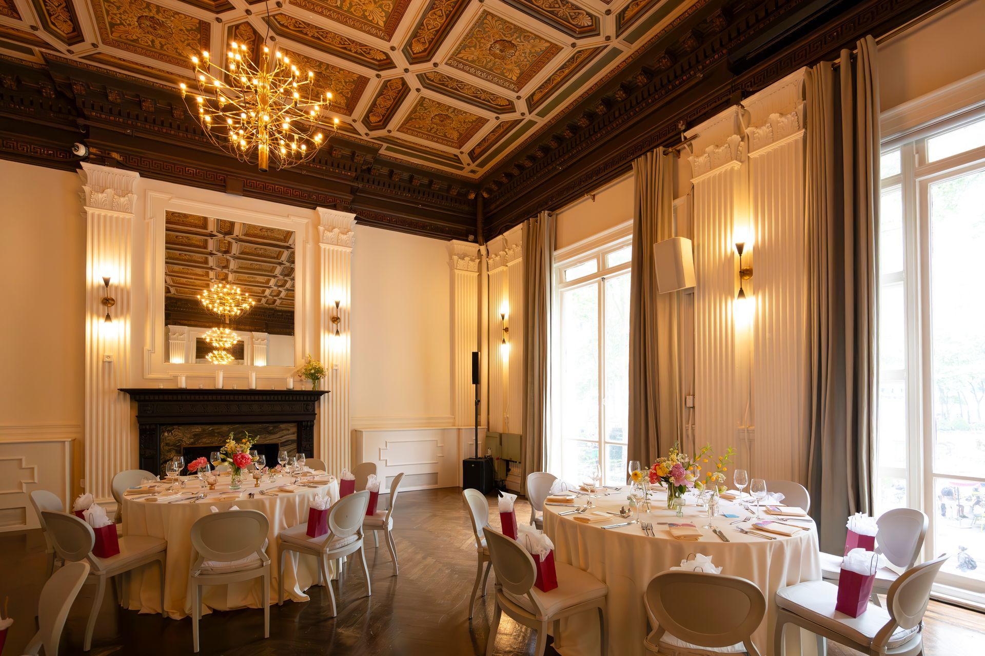 Elegant banquet hall with round tables, white tablecloths, gold accents, and tall windows casting warm light