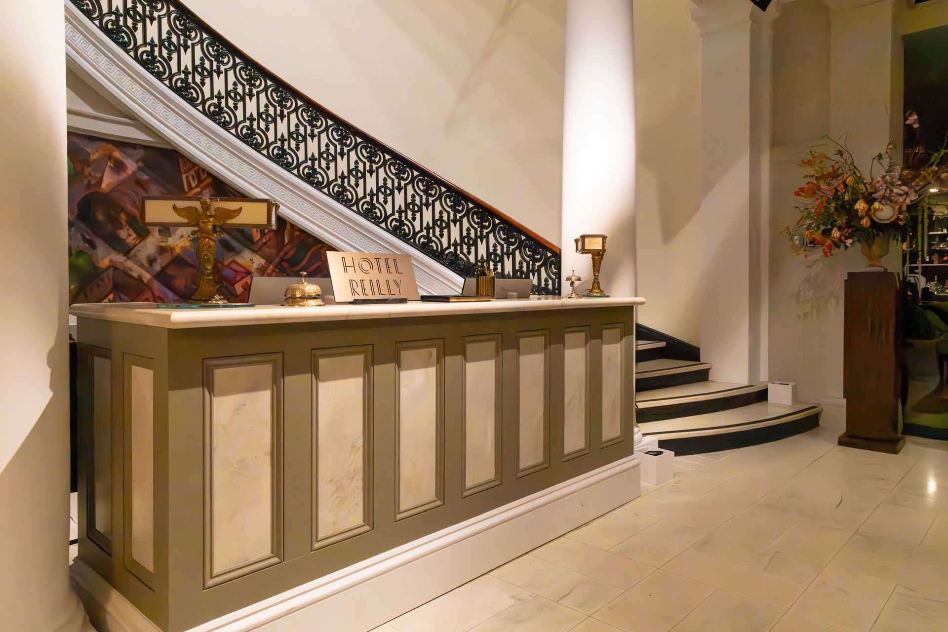 Hotel lobby with front desk, staircase, and marble floor in warm lighting