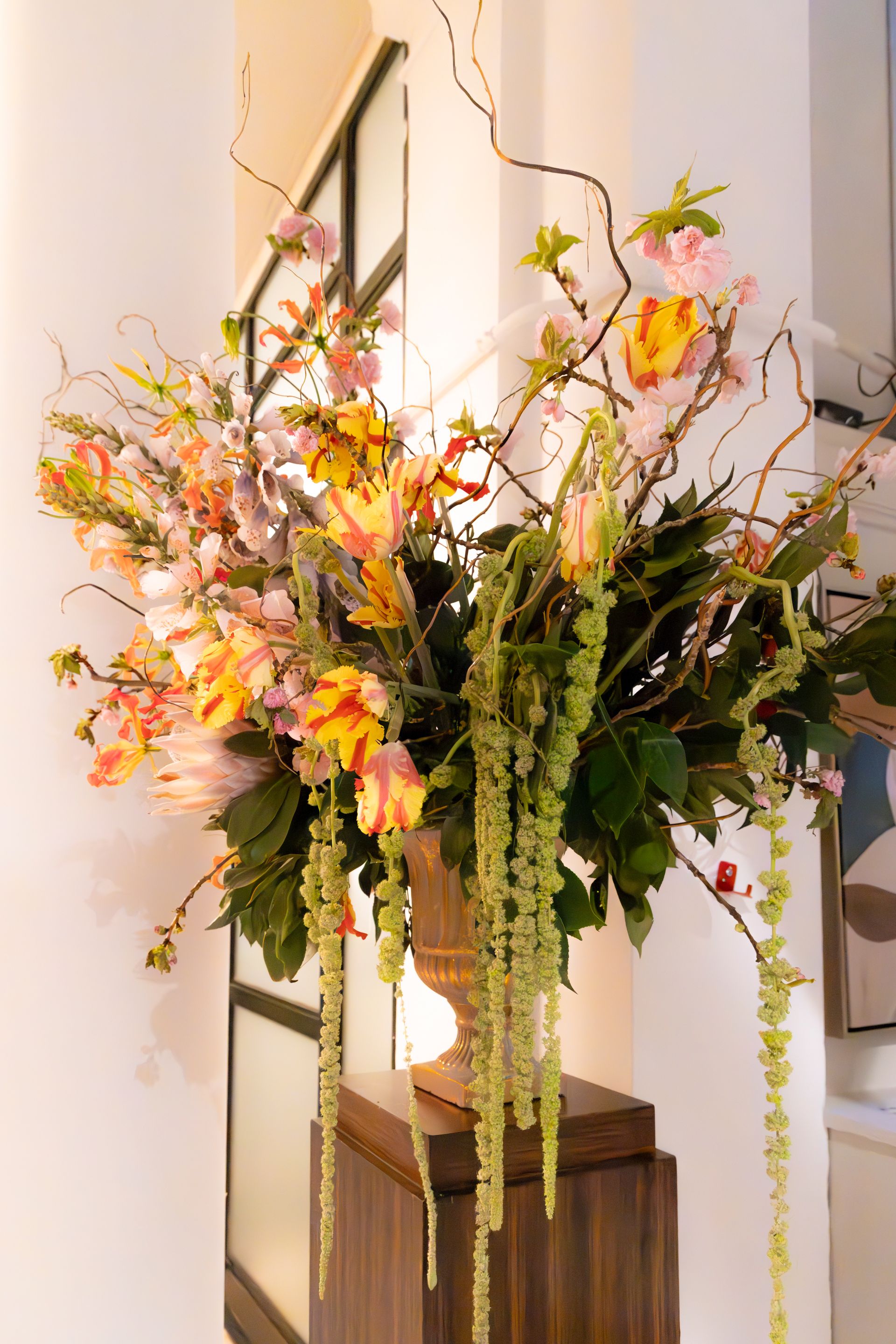 Tall floral arrangement with pink, yellow, and white blossoms in a vase on a pedestal indoors