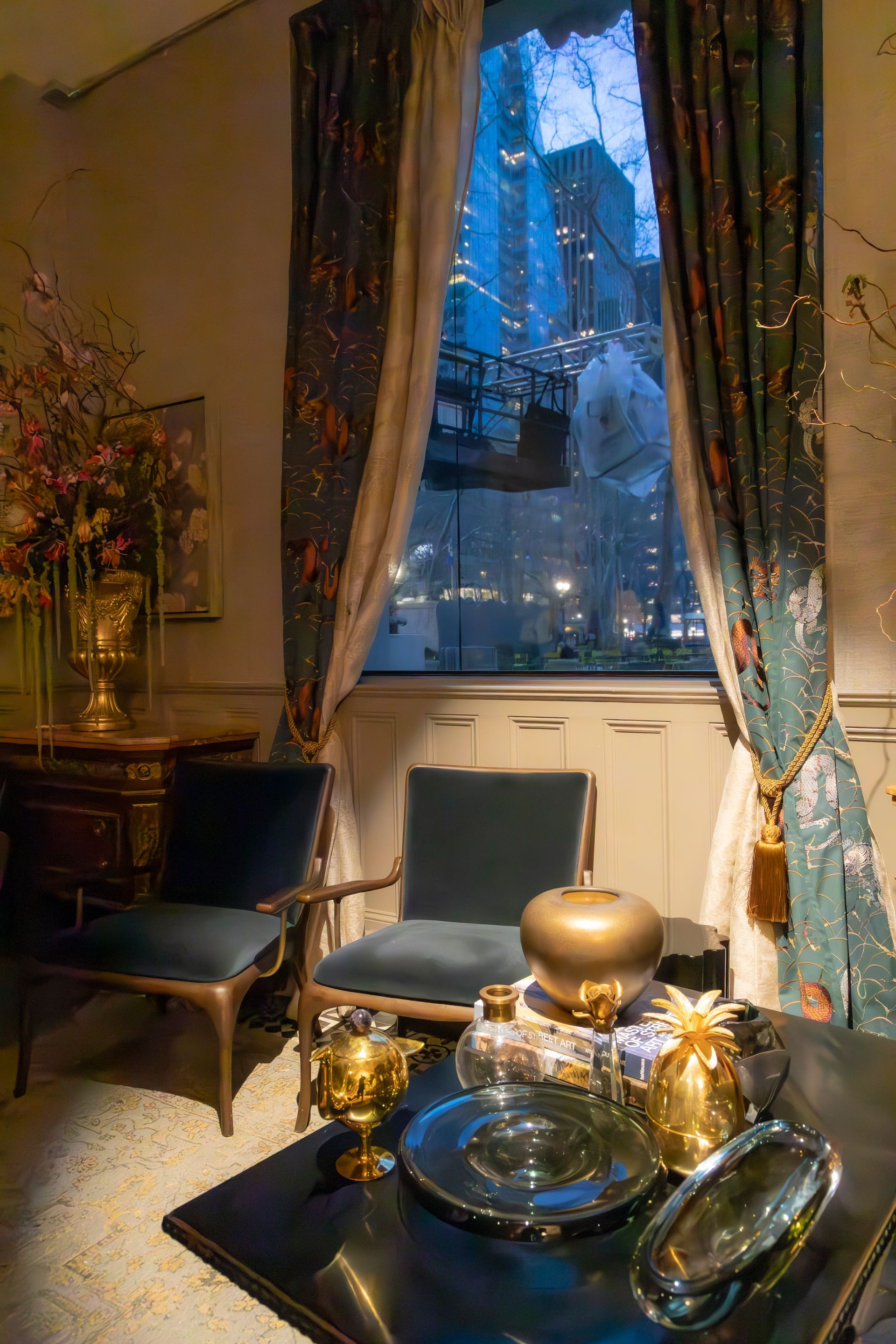 Elegant living room with dark blue chair, gold decor, and tall window framed by patterned curtains.