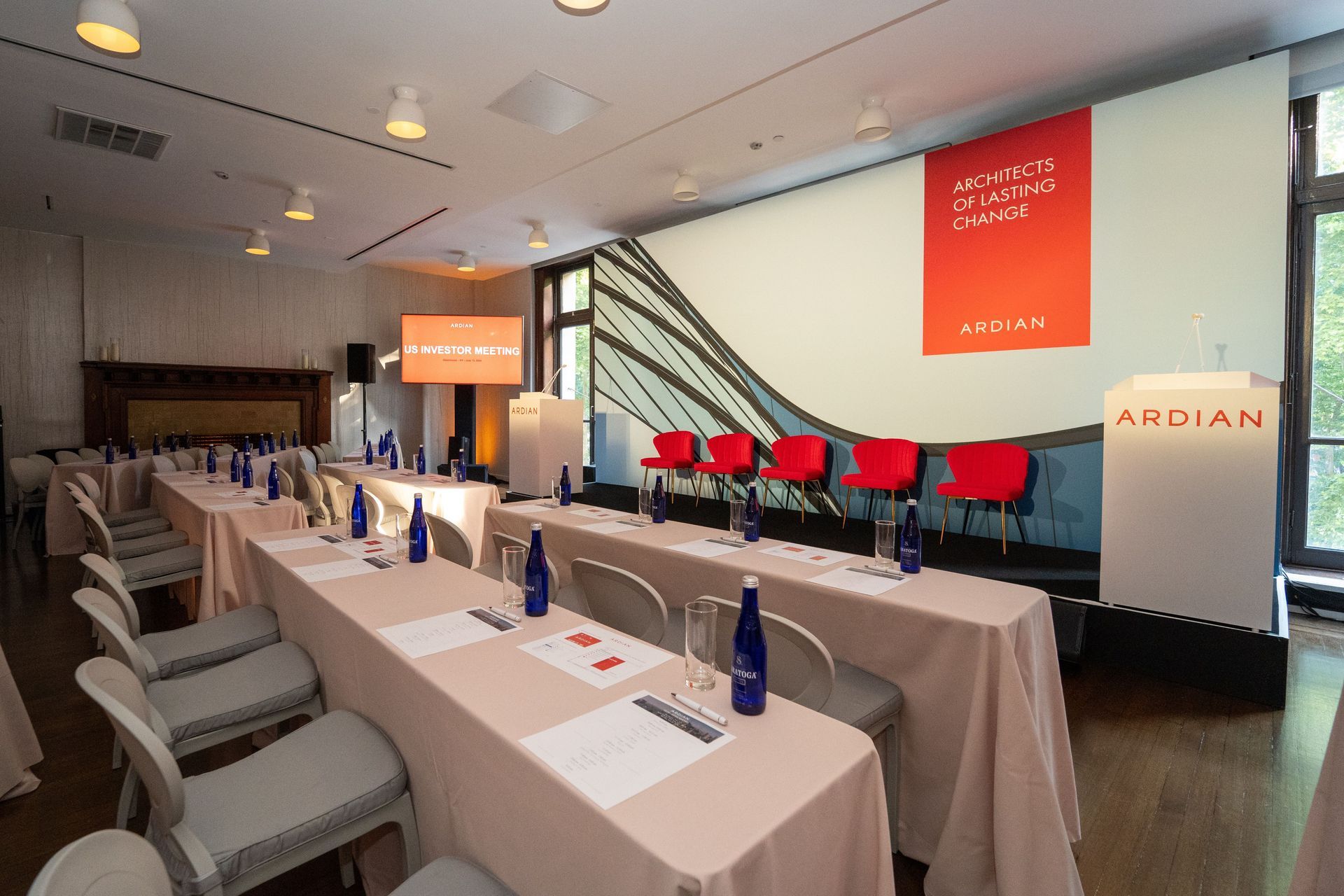 Conference room with long tables, red chairs on a stage, and orange presentation banners on the wall
