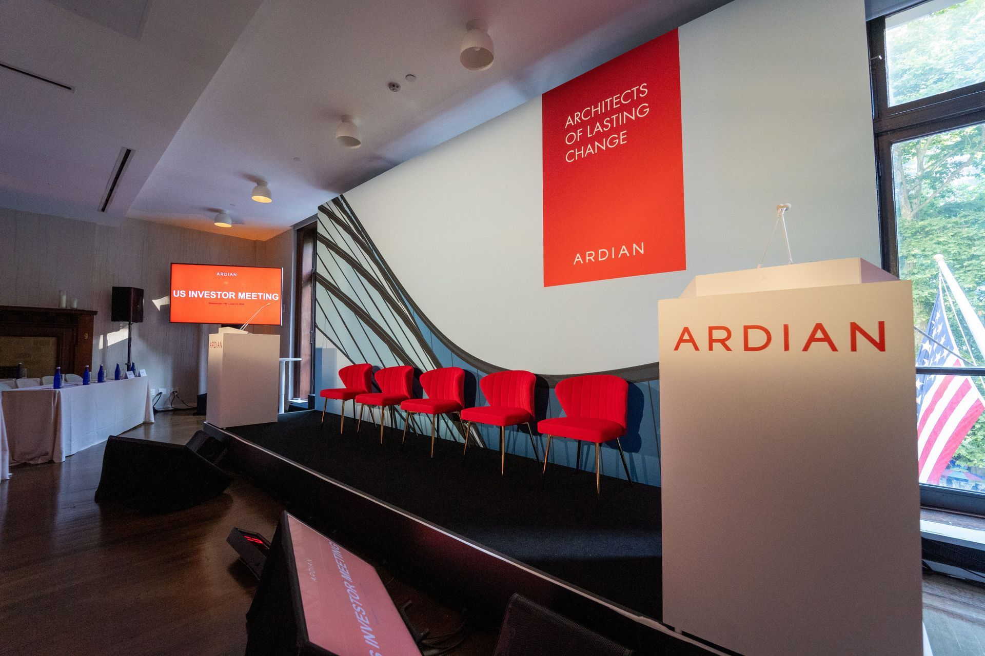 Conference stage with red chairs and ARDIAN sign in a modern office lobby.