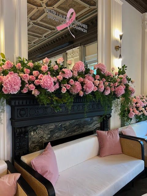 Pink floral arrangement on a black fireplace mantel above a white sofa with pink pillows in a mirrored room