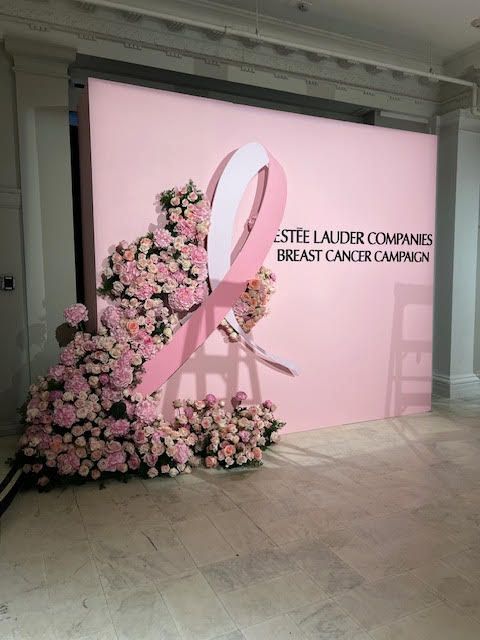 Pink breast cancer awareness display with a ribbon and flowers beside a wall sign