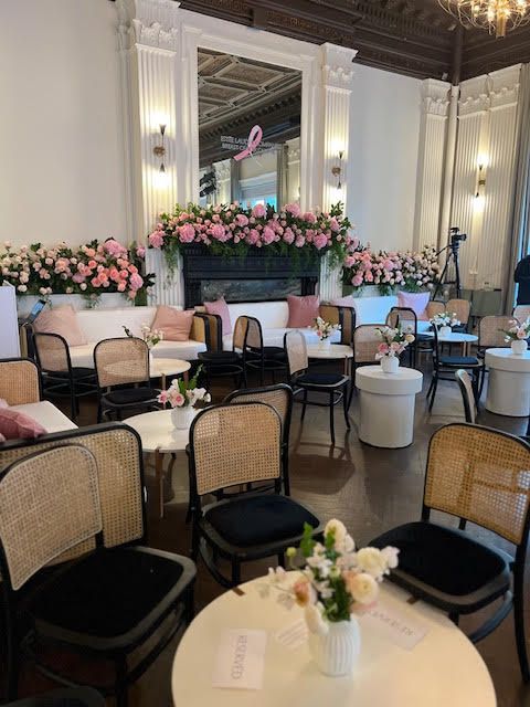 Elegant event hall with pink floral stage backdrop and round tables with cane chairs