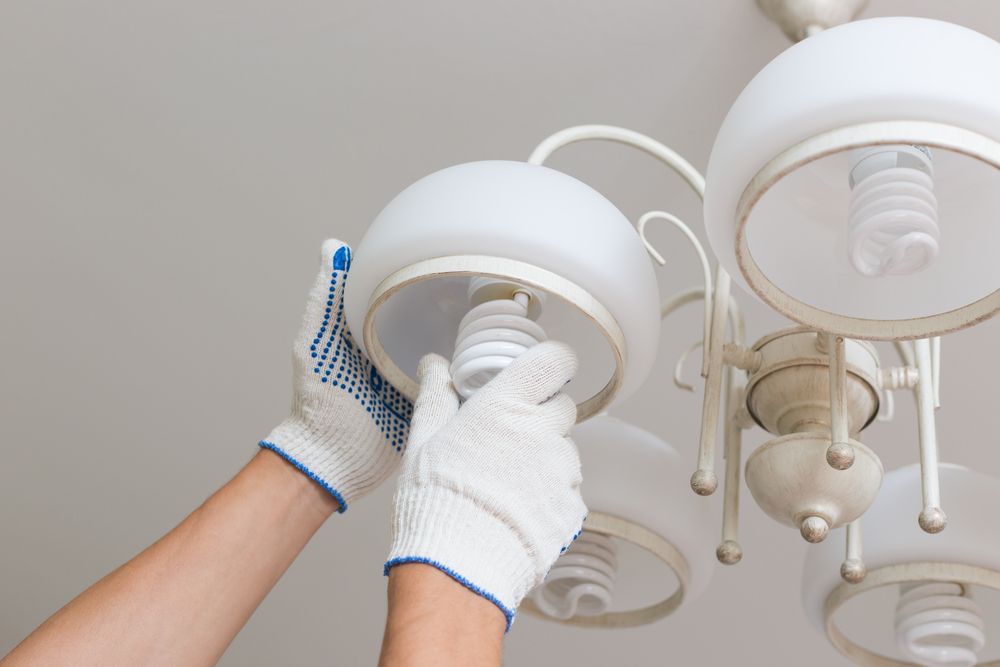 A Person is Changing a Light Bulb in a Chandelier — Coppo's Electrical in Helensvale, QLD