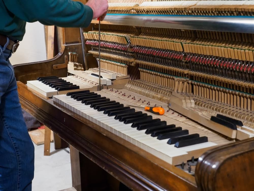 A Man Is Working on A Piano with A Screwdriver — Tony Prince Piano Tuning In Kempsey, NSW