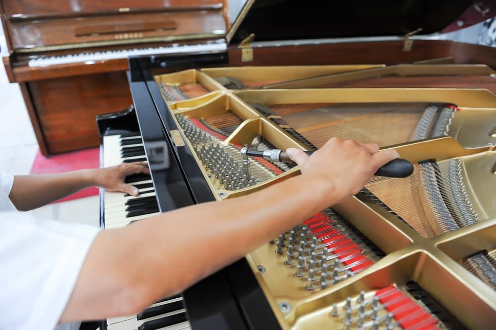 A Person is Working on a Piano With a Wrench — Tony Prince Piano Tuning In Taree, NSW