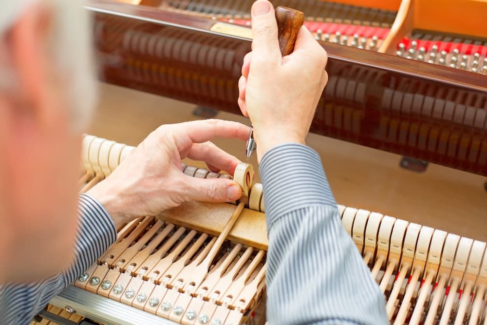 A Man Is Working on A Piano with A Screwdriver — Tony Prince Piano Tuning In Taree, NSW