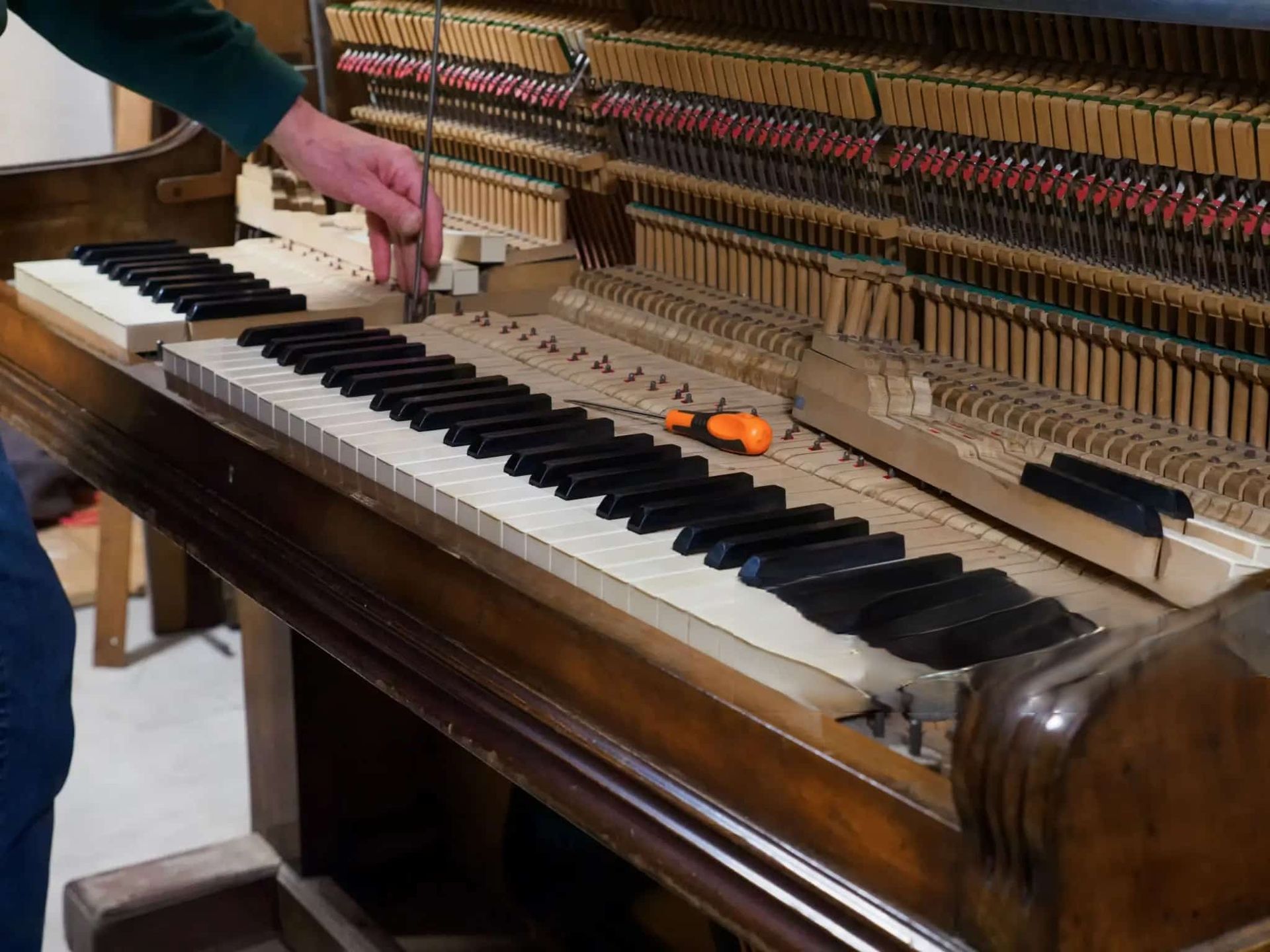 A Person Is Working on A Piano with A Screwdriver — Tony Prince Piano Tuning In Taree, NSW