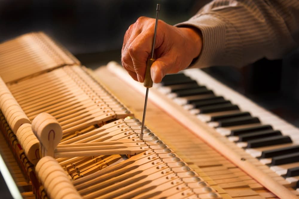 A Person Is Working on A Piano with A Screwdriver — Tony Prince Piano Tuning In Taree, NSW