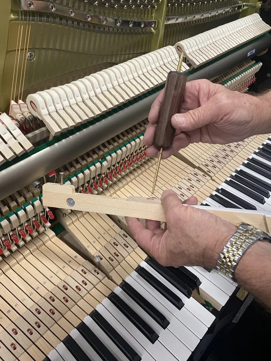 A Person Is Holding a Wooden Stick in Front of A Piano Keyboard — Tony Prince Piano Tuning In Taree, NSW