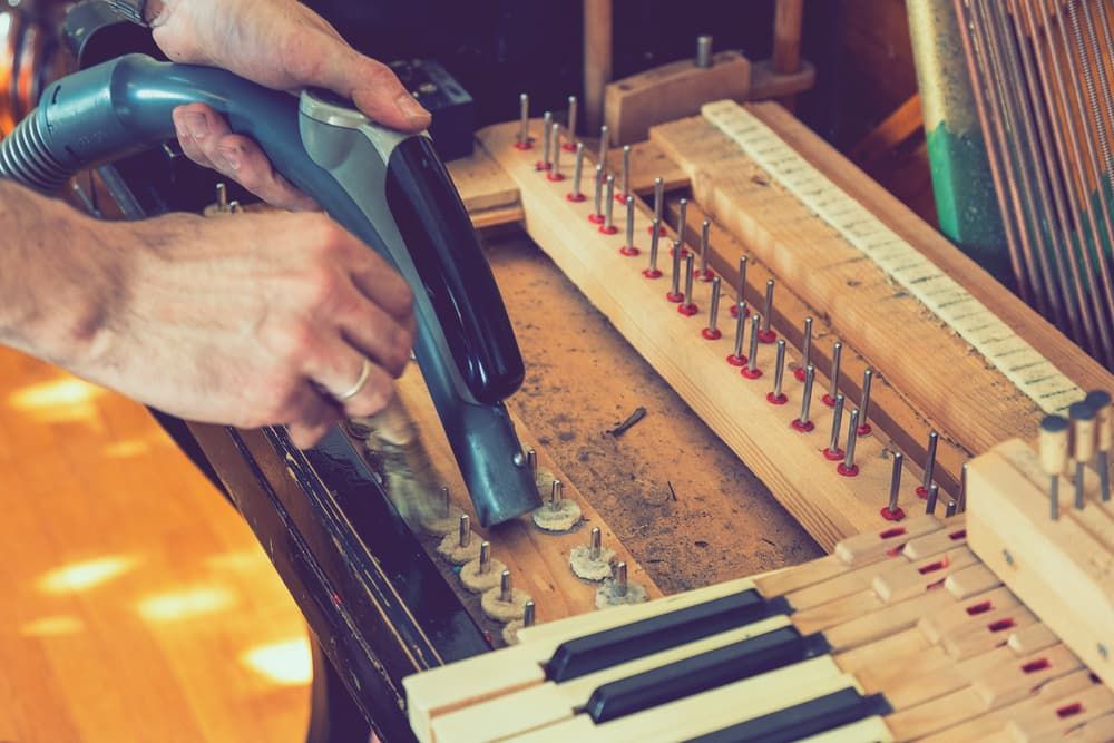 A Person Is Cleaning a Piano with A Vacuum Cleaner — Tony Prince Piano Tuning In Taree, NSW