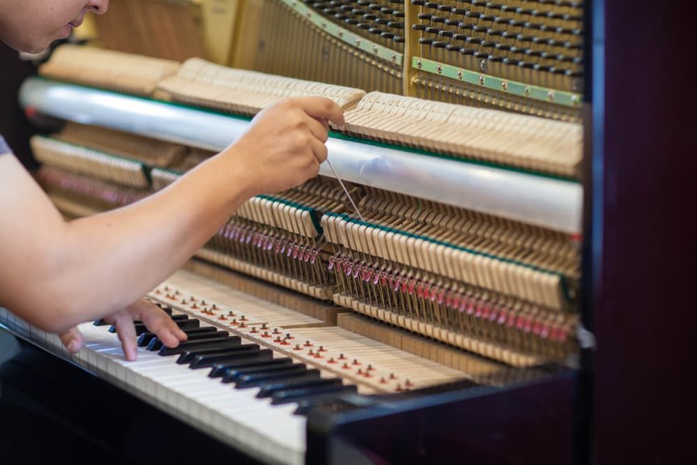 A Person Is Working on A Piano with A Screwdriver — Tony Prince Piano Tuning In Forster, NSW
