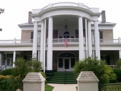 A stately, two-story colonial revival home with a grand white pillared portico, a balcony, and front steps.