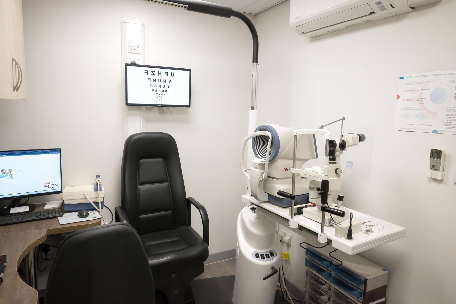 Optometry exam room with equipment, eye chart, and chair.