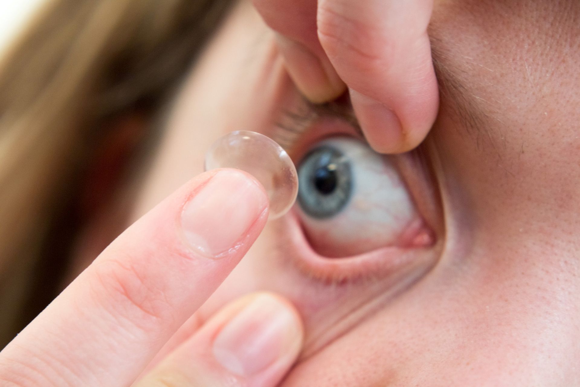 Person inserts a clear contact lens into a blue eye.