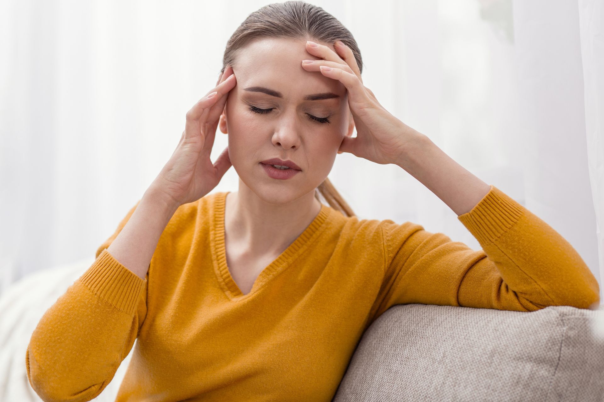 Woman in yellow shirt suffers from a headache.