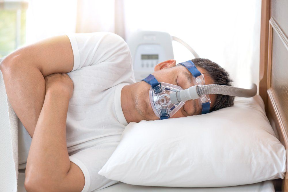 Man with a CPAP machine sleeps on his side with the mask on his face.