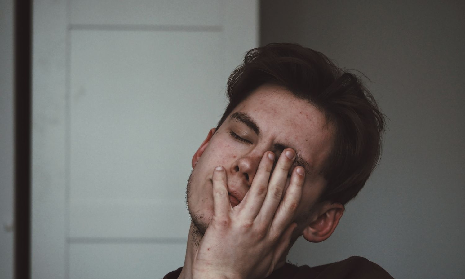 Man with brown hair with his hand covering half of his face from jaw pain.