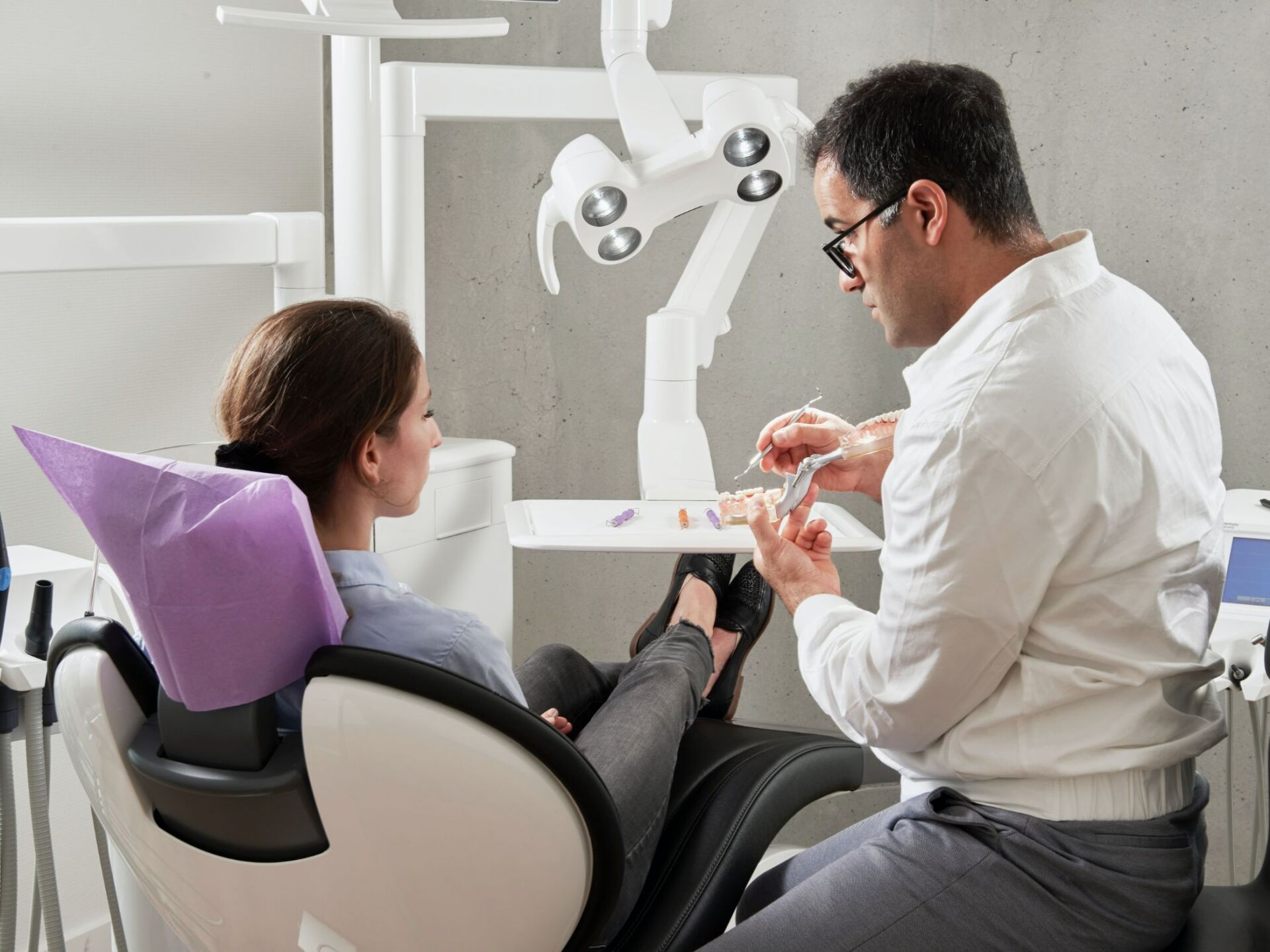 TMJ doctor demonstrates on model teeth to a female patient in a doctor's chair.