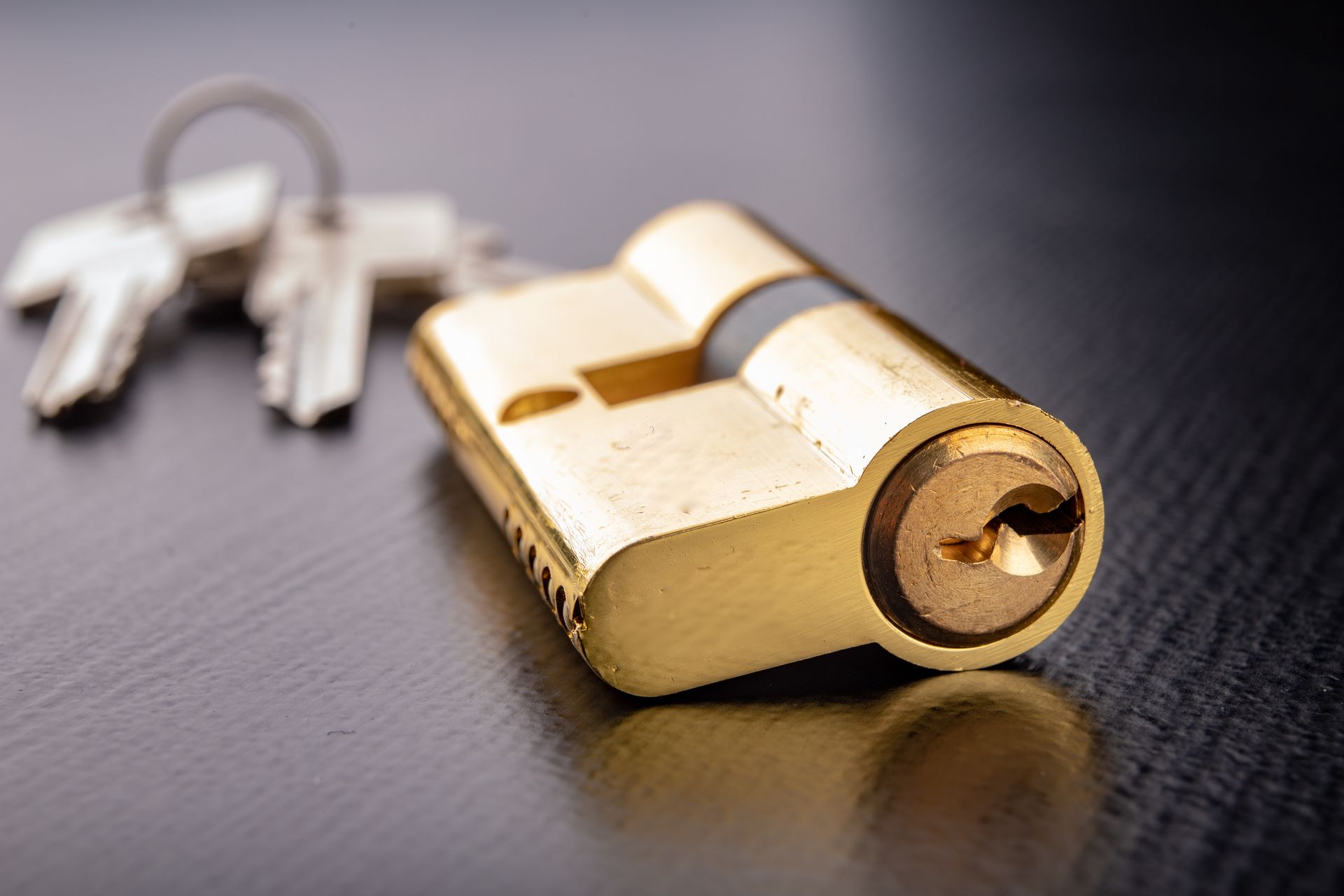 Gold lock with two silver keys on a dark surface
