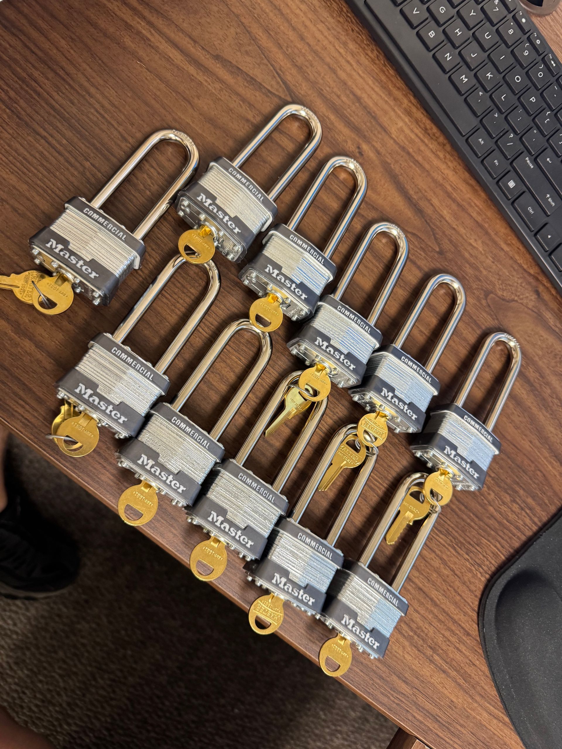 Seven silver padlocks with yellow tags arranged on a wooden table near a keyboard.