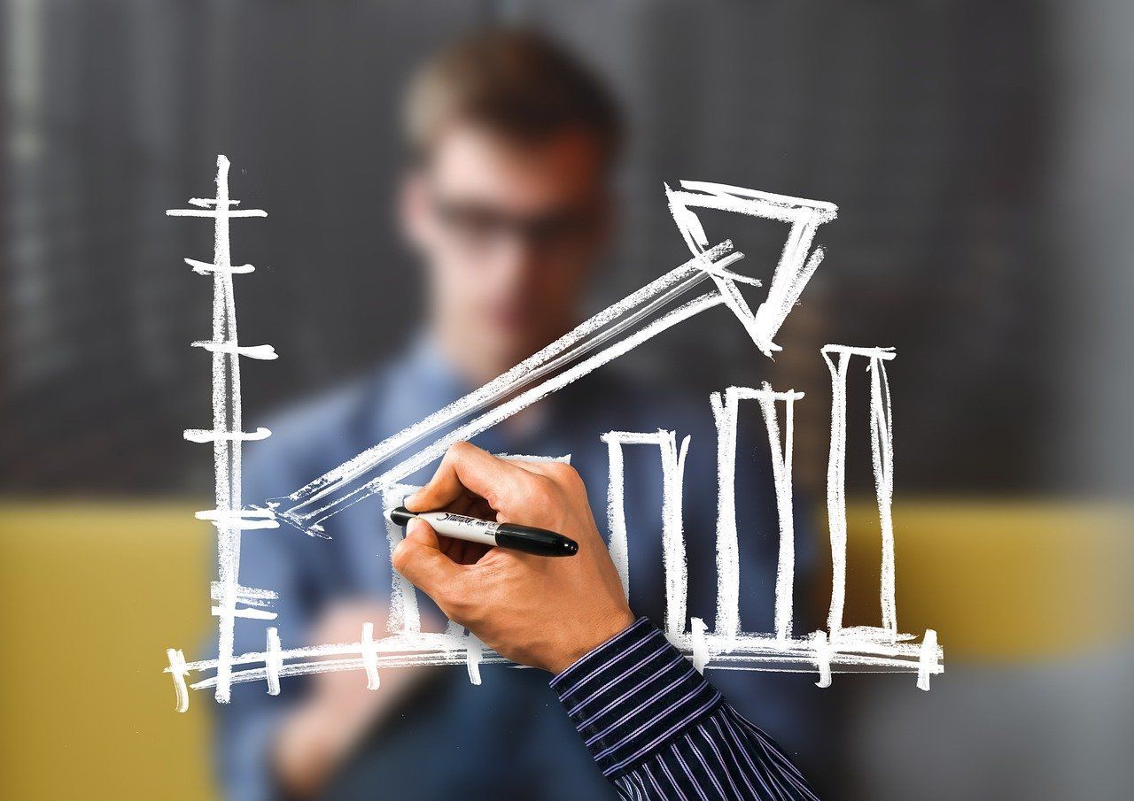 Person drawing a rising bar graph with a white marker, likely indicating growth or success.
