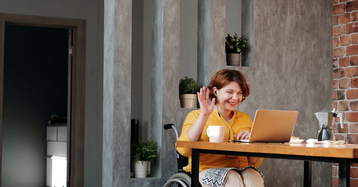 A woman in a wheelchair is sitting at a table using a laptop computer.