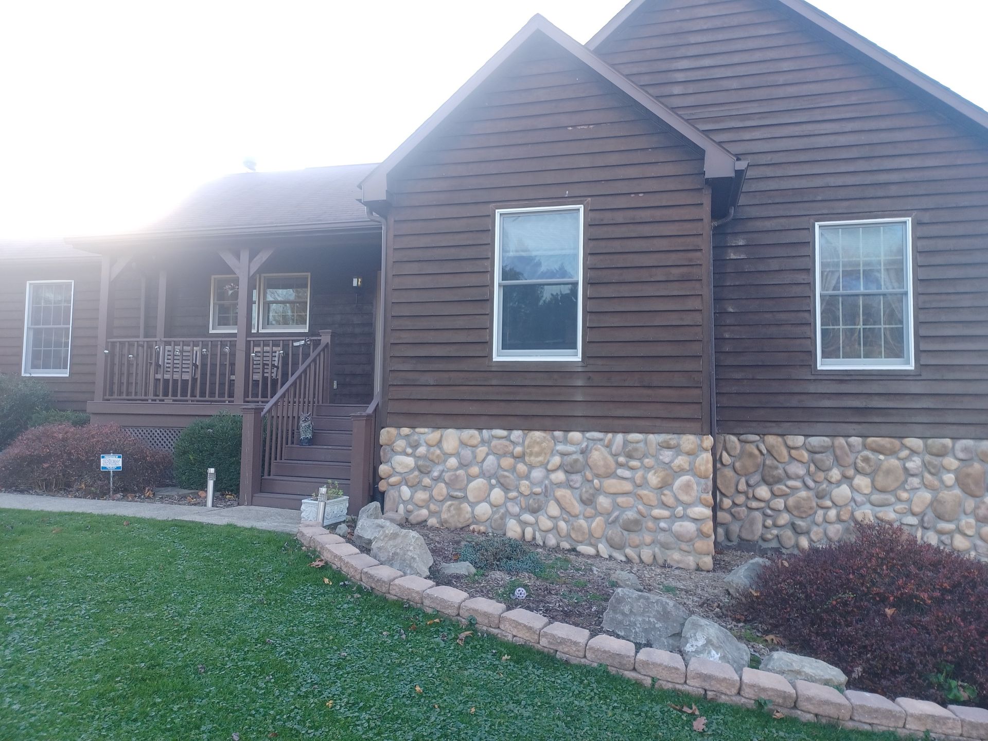 A brown house with a stone foundation and a porch