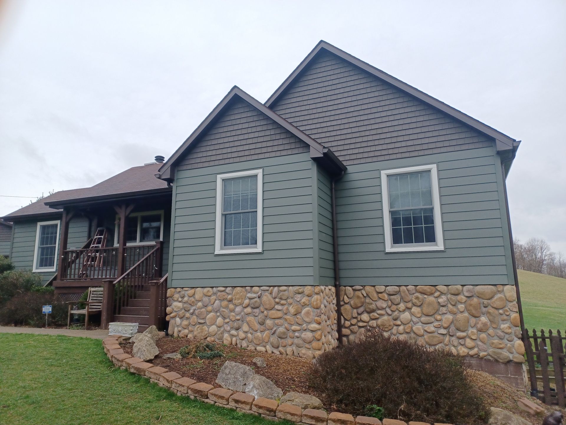 A large house with a stone foundation and a green siding.