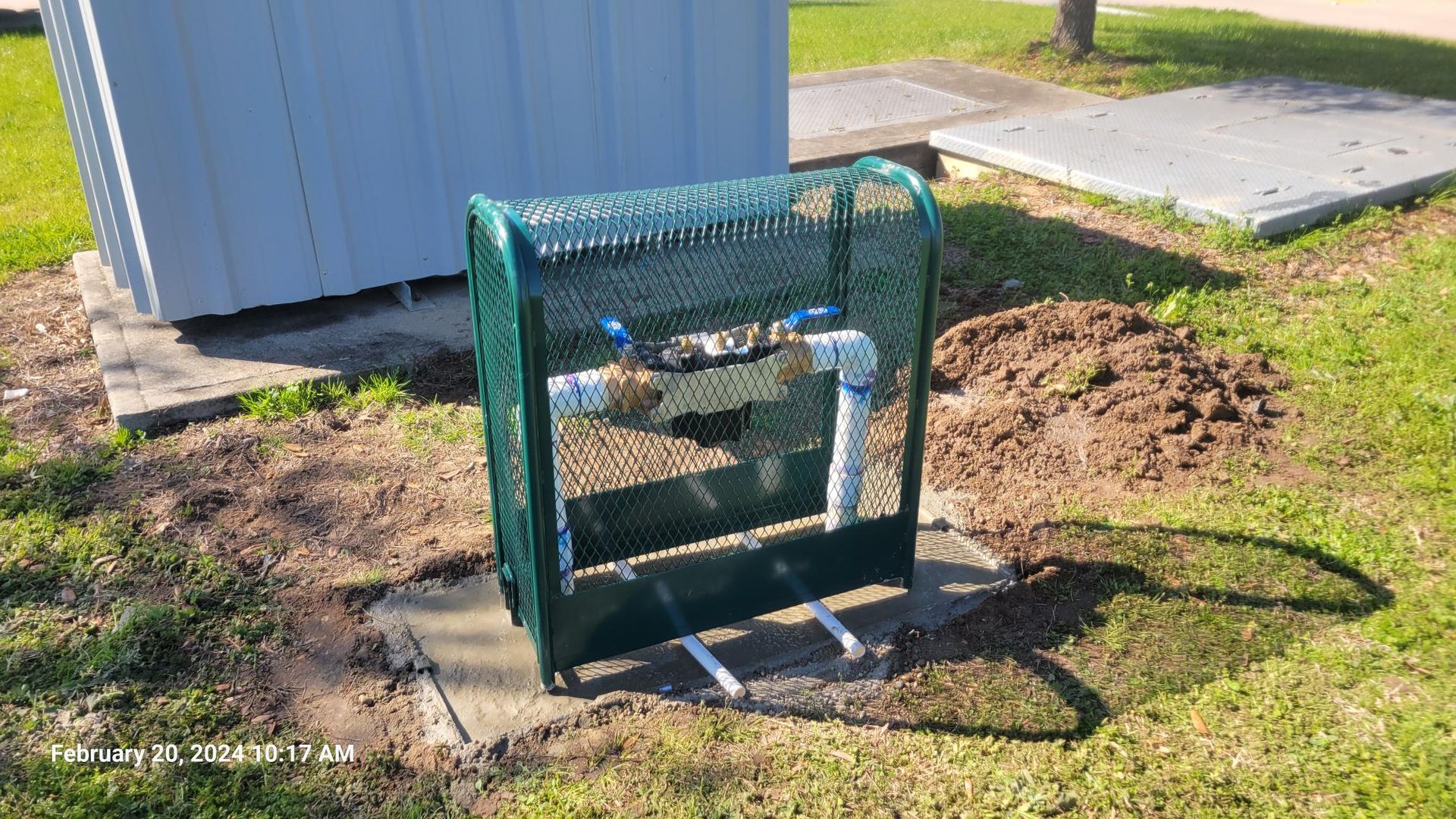 A water meter is sitting in the grass next to a building.