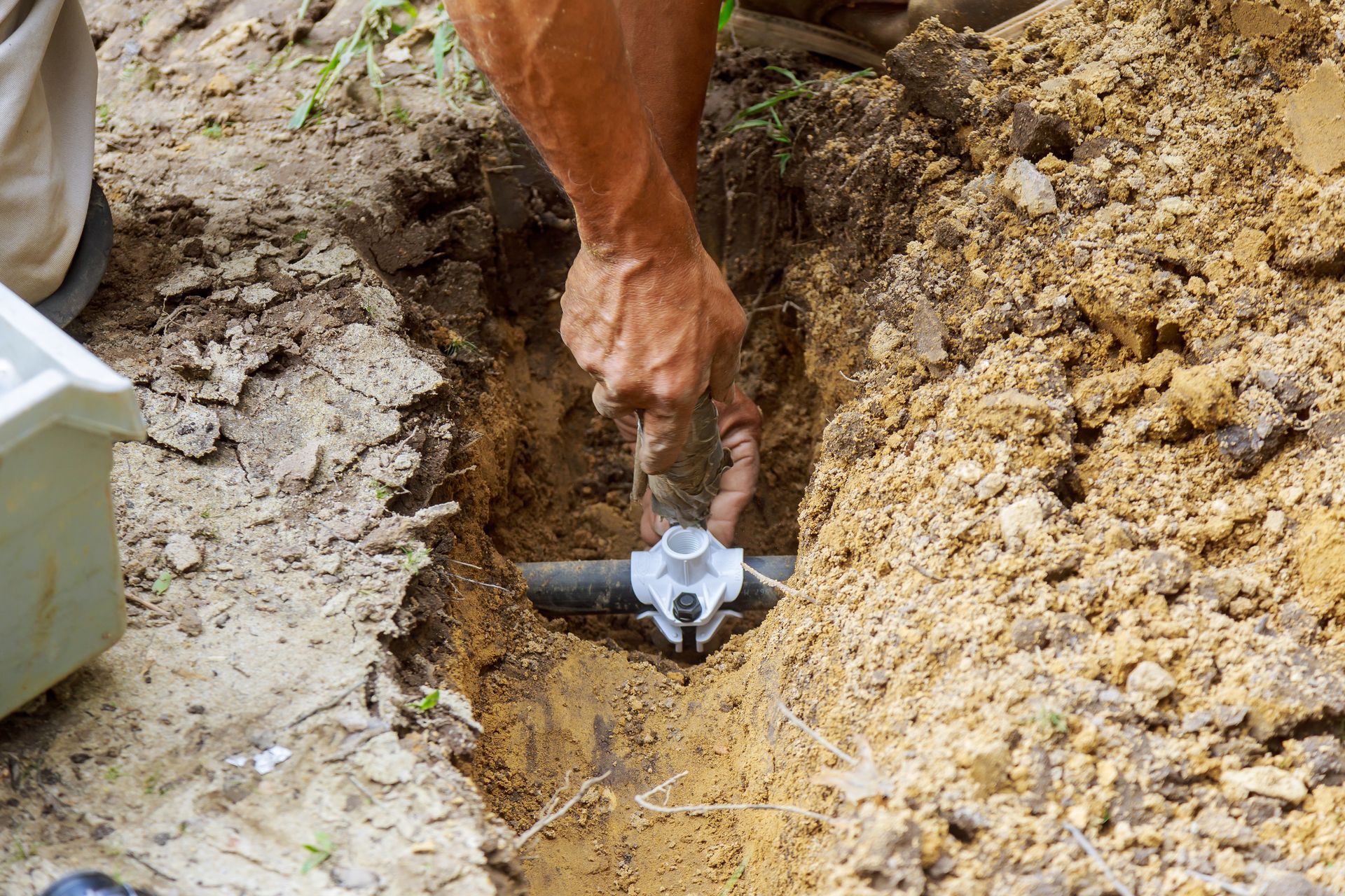 A man is fixing a pipe in the dirt.