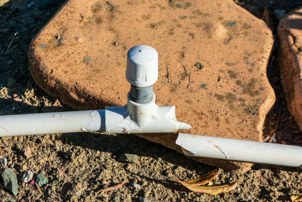 A broken pipe is sitting on the ground next to a rock.