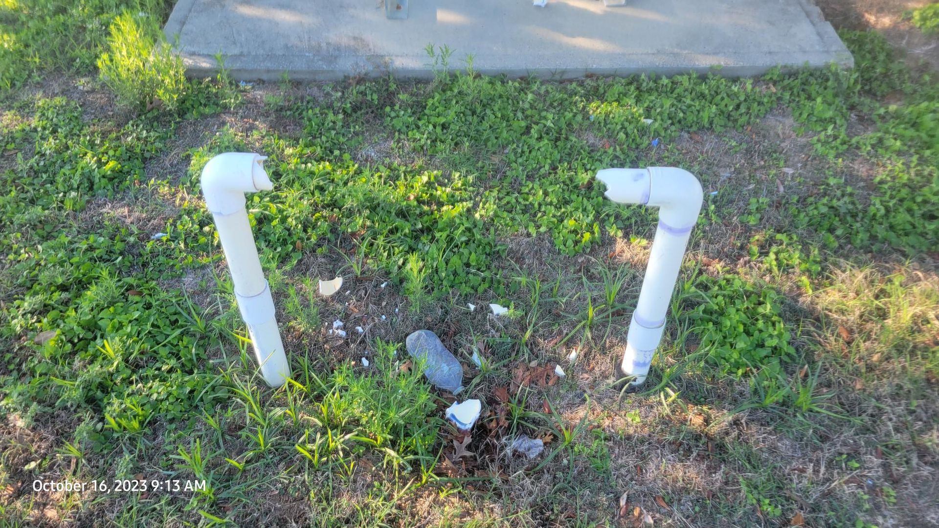 Two white pipes are sitting in the grass next to a concrete slab.
