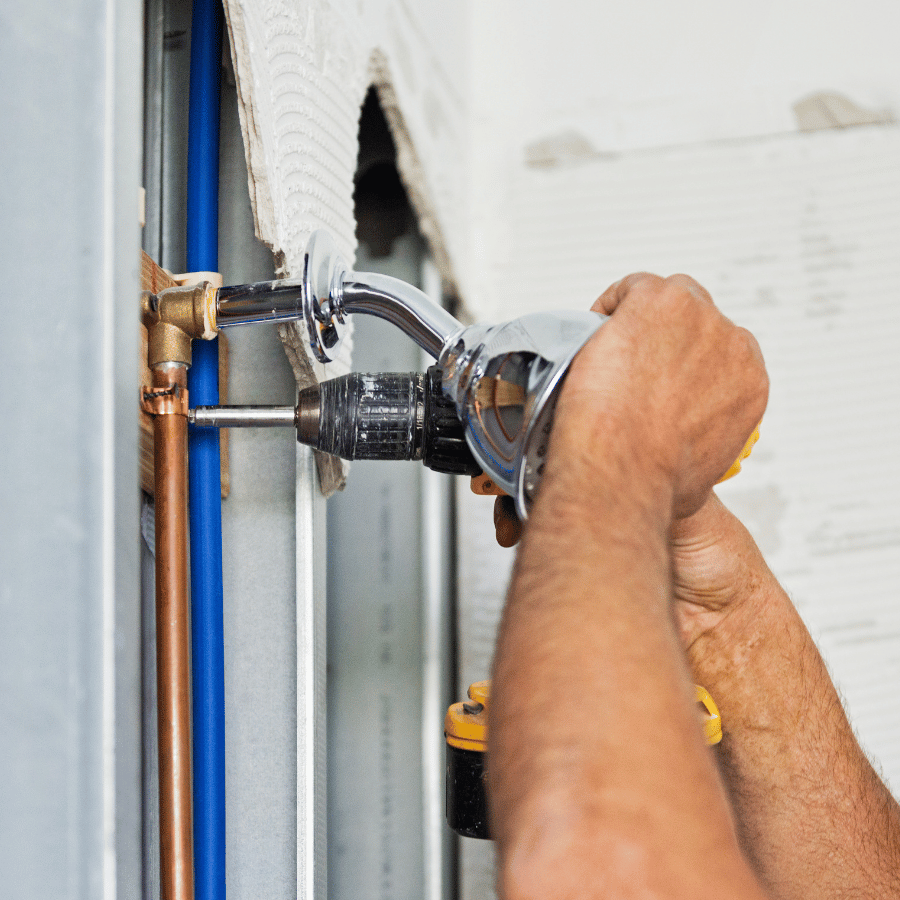 Plumber tightening a pipe fitting with a wrench on a wall-mounted water line