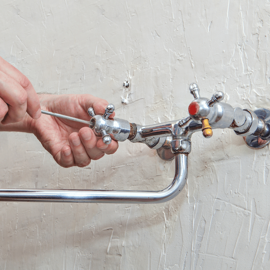 Hand adjusting a chrome faucet handle on exposed plumbing against a textured wall