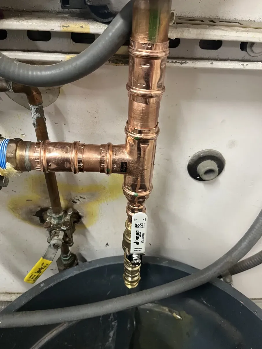 Copper plumbing pipes above a bucket, with a gray hose and a small shutoff valve below.